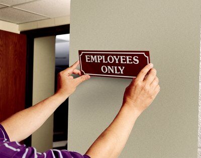Hands putting “Employees Only” sign on a door using double coated tape